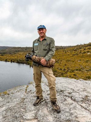Peter Rowland standing on a rocky ledge with Tasmania's Dove Lake in the background